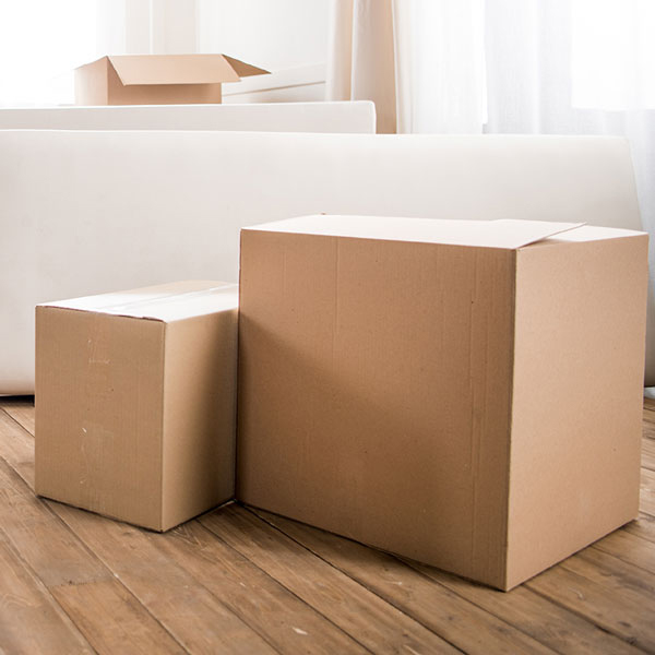 Boxes on the floor in a home. with a white sofa and a partly rolled rug. Soft, daylight shines through the white curtains.