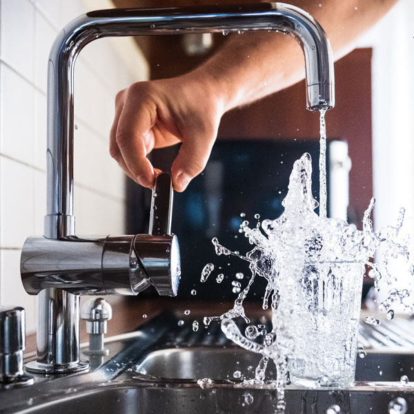 A hand turns on the water from a stainless steel kitchen faucet sink at a brownstone apartment in Brooklyn. The water splashes up to fill a large glass.